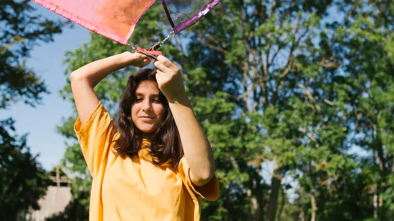 Flicka håller står utomhus i gul t-shirt och håller i två tyger som svävar i vinden ovanför hennes huvud.