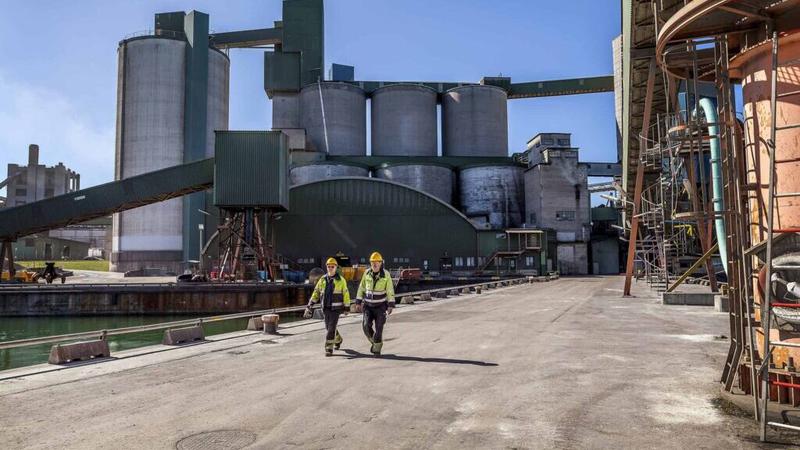 Två män går längs en väg intill en fabrik.
