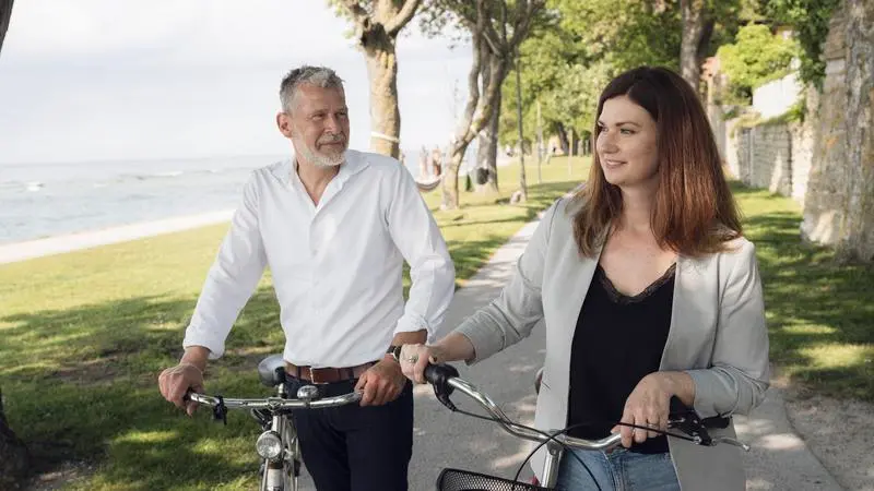 En man och en kvinna leder var sin cykel längs en gångväg vid havet