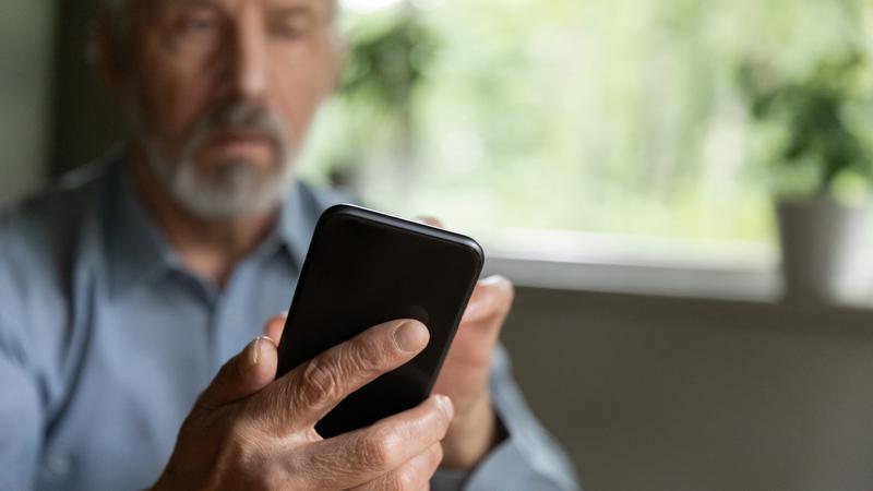 Äldre man håller i en mobiltelefon