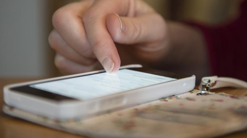 En användare pekar på en mobiltelefon, visar en närbild på mobil och fingret som trycker på den.