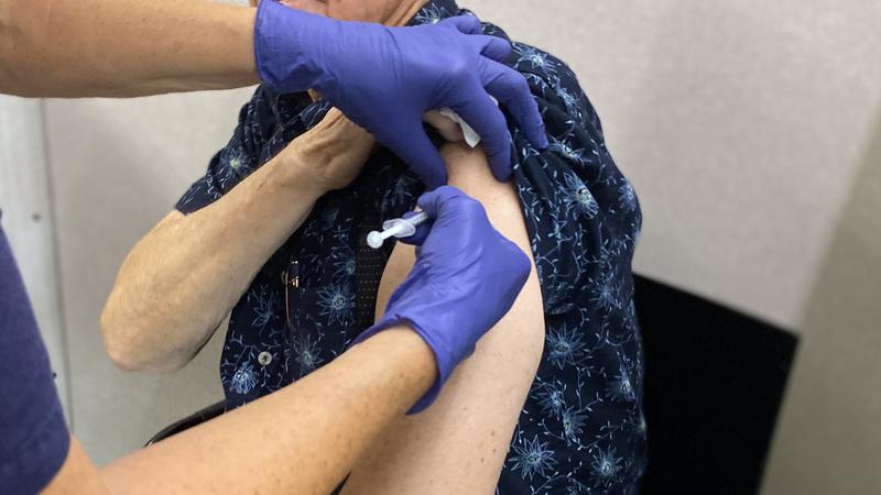 Äldre man blir vaccinerad. Har dragit upp skjortärmen.