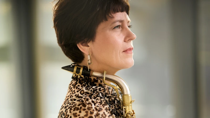 En kvinna i leopardmönstrad skjorta håller i en saxofon.