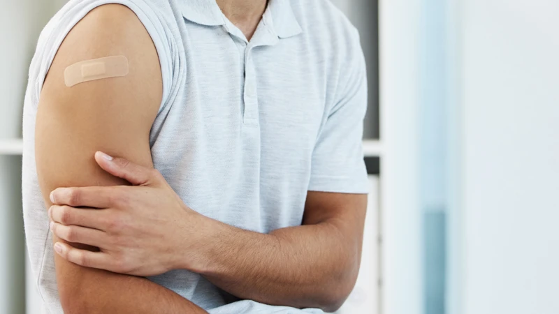 En person sitter på en stol och har plåster på överarmen efter vaccination.
