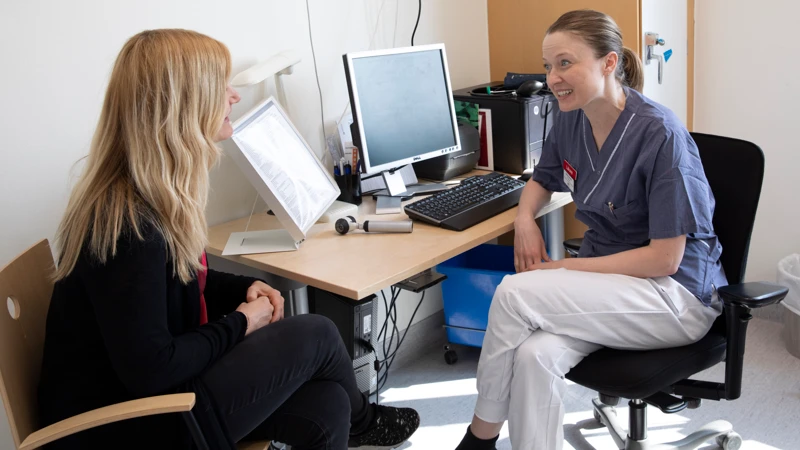 En läkare sitter vid ett skrivbord och pratar med en patient..