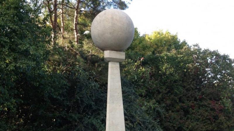 Framför en skog syns ett stort klot av sten på en pelare