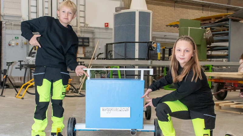 Två barn i arbetskläder visar upp en låda med texten Byggkollo 2026.