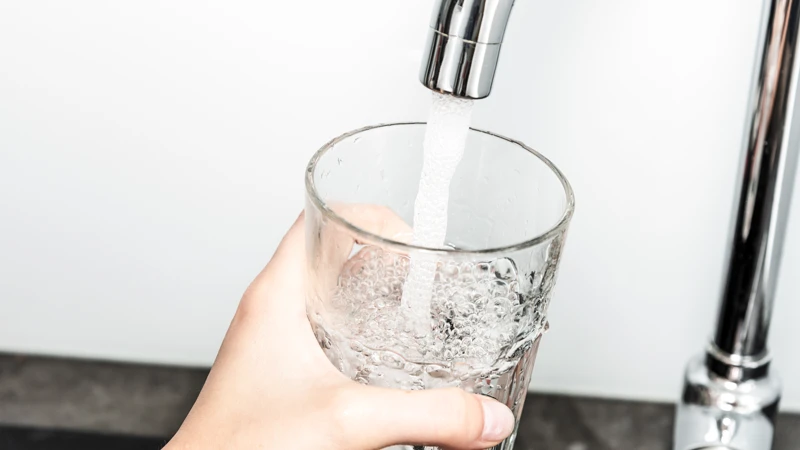 En person som håller ett glas vatten under en kran.