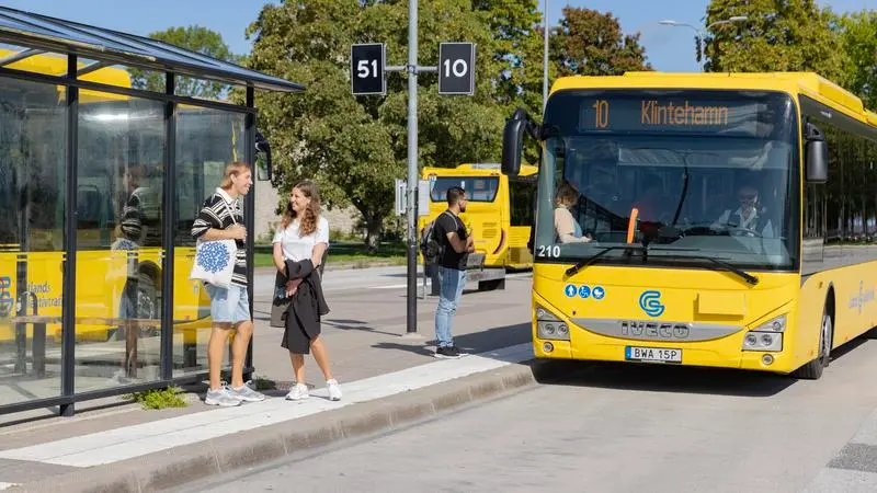 Busshållplats med personer som väntar och en gul buss