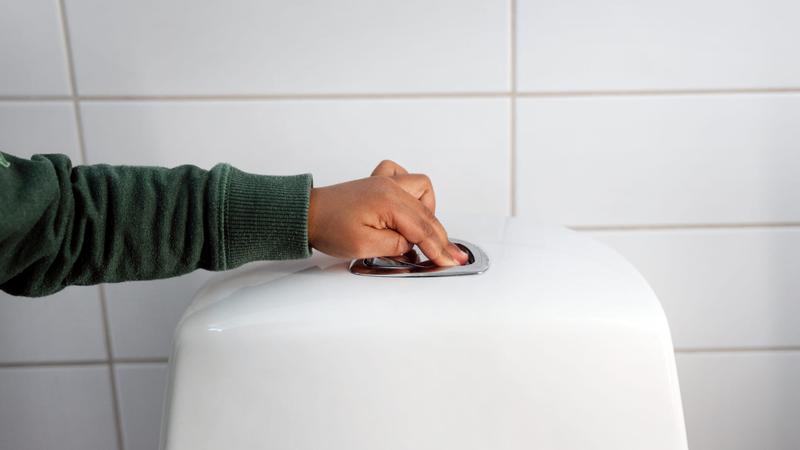 Hand som trycker på spolknappen på toalett