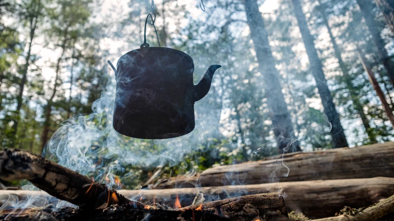En kaffekanna som hänger över en lägereld i skogen.