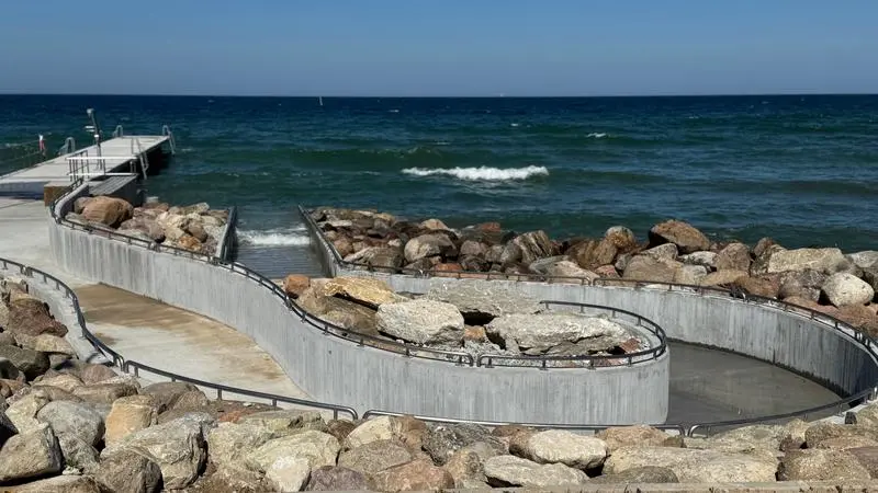 Badbrygga med en gångväg i betong som leder ner till havet.