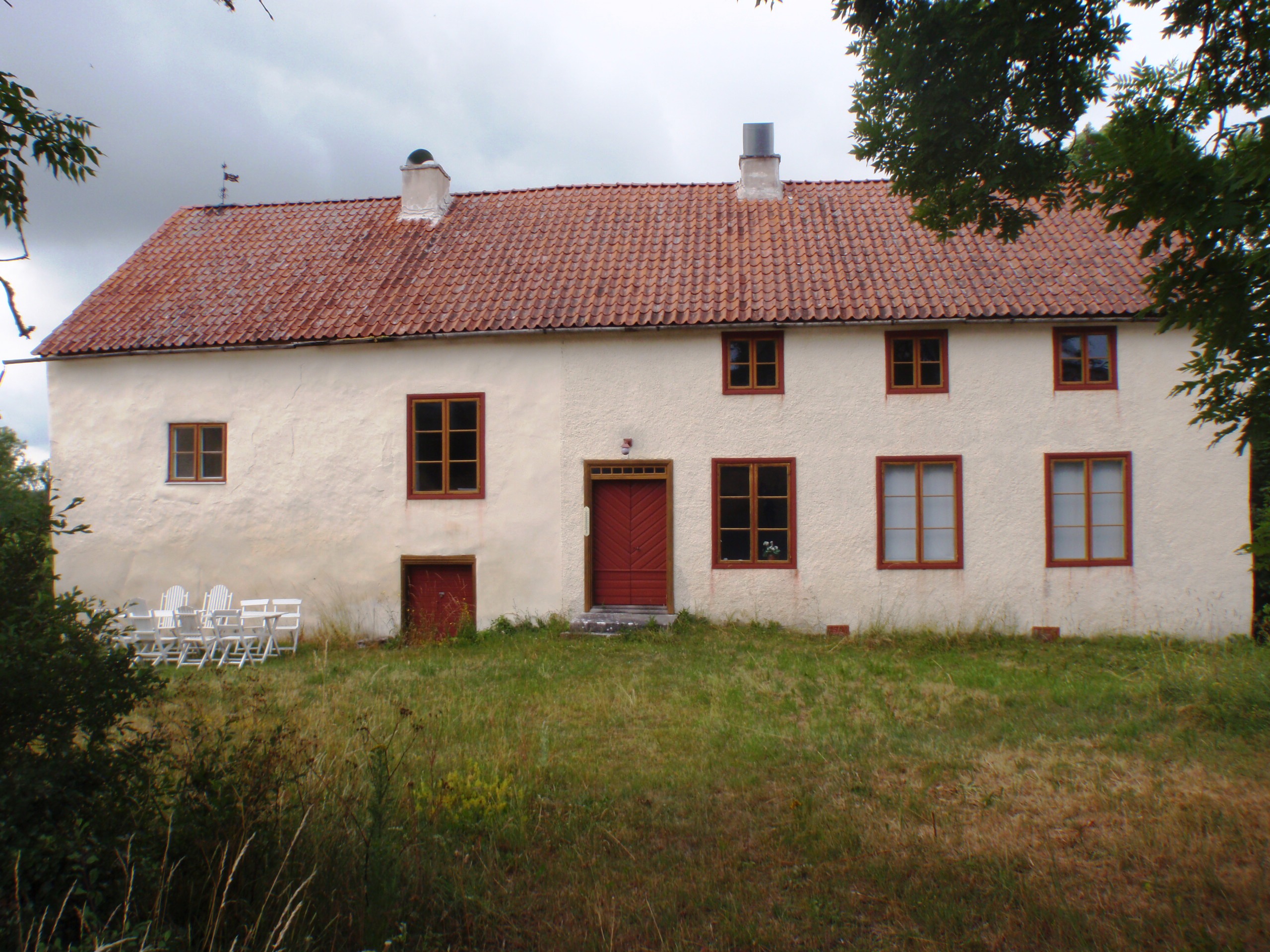 Ett ljusrosa hus bestående av två våningar har ett rött tak, bruna fönster och en röd ytterdörr.