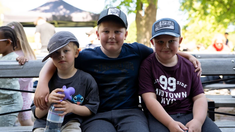 Tre barn med keps sitter på en bänk.