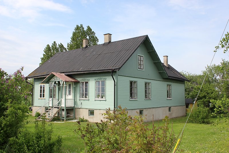 Ett grönt trähus med vita fönster, en vit ytterdörr och ett svart plåttak.