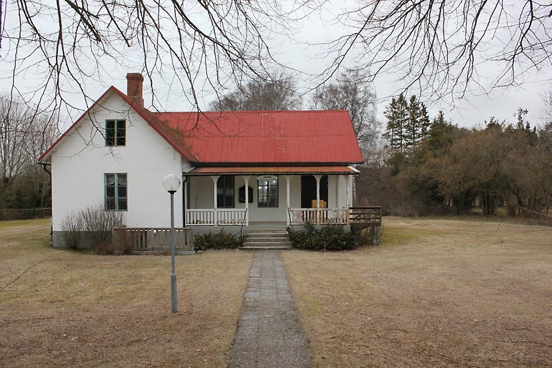 Ett vitt hus med en svart ytterdörr, gröna fönster och ett rött plåttak.