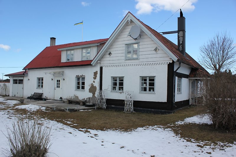 Ett vitt hus med ljusblåa fönster och ett rött tak.