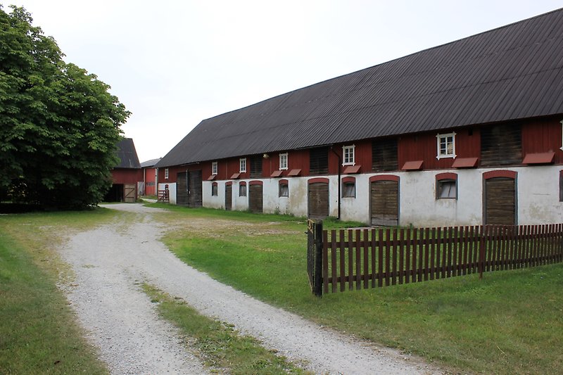 En rödvit lada med vita fönster, bruna dörrar och ett svart plåttak.