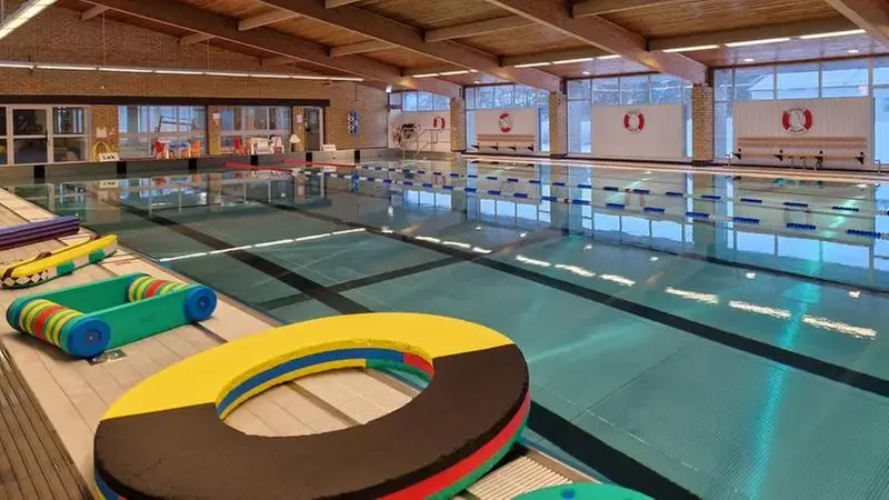 Simhall med stor bassäng och flytleksaker på bassängkanten.