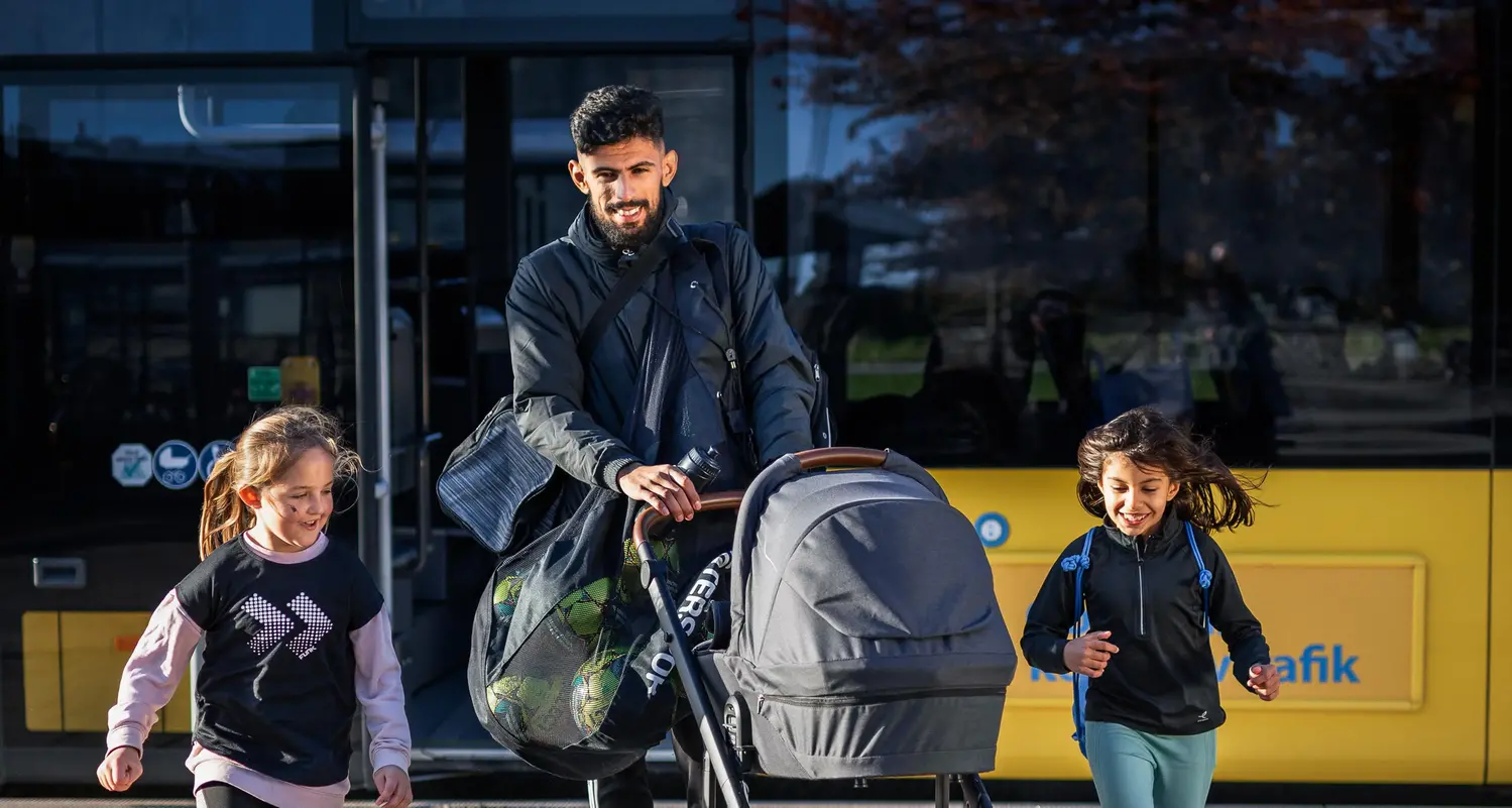 Pappa med två barn och en barnvagn utanför bussen