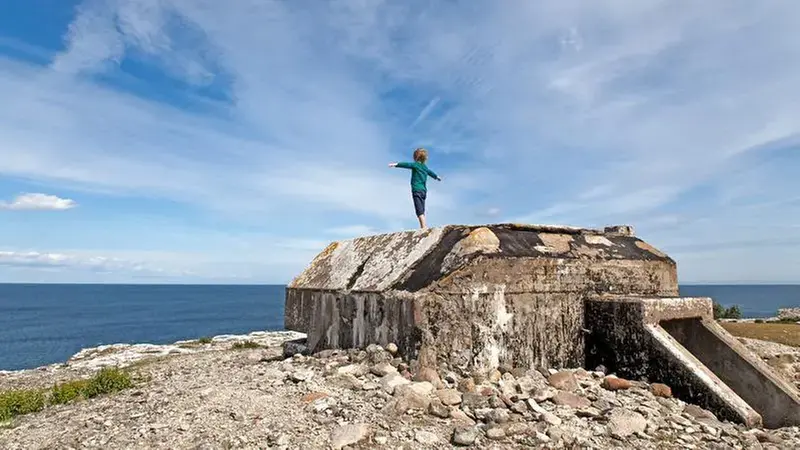 Ett barn står på ett betomgfundament och ser ut över havet