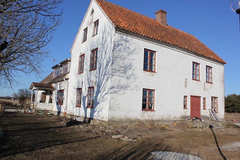 Ett stort vitt hus med orange tak, en skorsten, bruna fönster och röd ytterdörr.