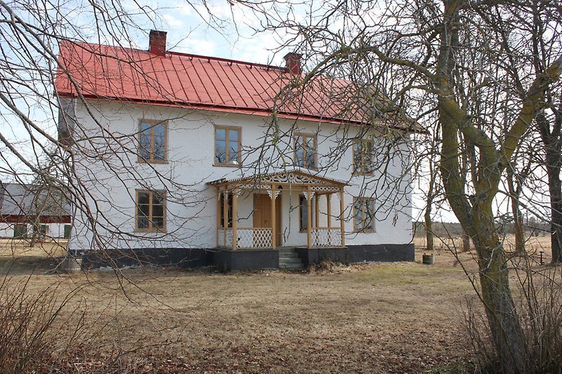 Tvåvånings hus med ett rött tak, två skorstenar och bruna fönster.