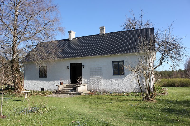 En nybyggd stuga med vita väggar, svart tak, svart ytterdörr och blåa fönster.