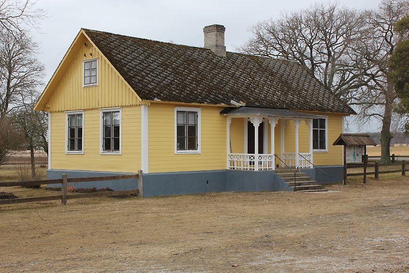 En gul envåningsbyggnad med bruna fönster, vita fönsterramar och en svart ytterdörr.