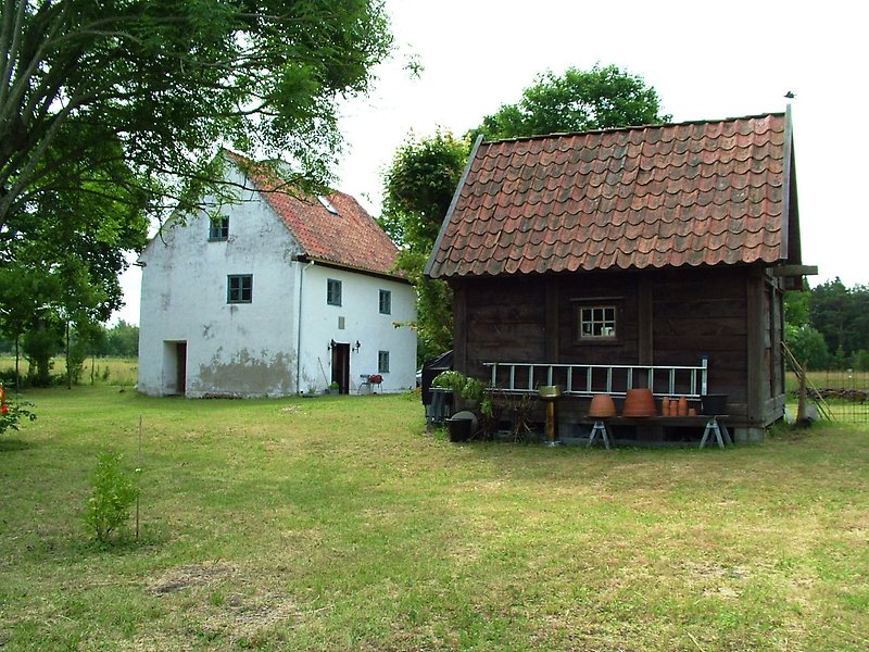 Ett vitt hus med blåa fönster och en trästuga med orange tak.