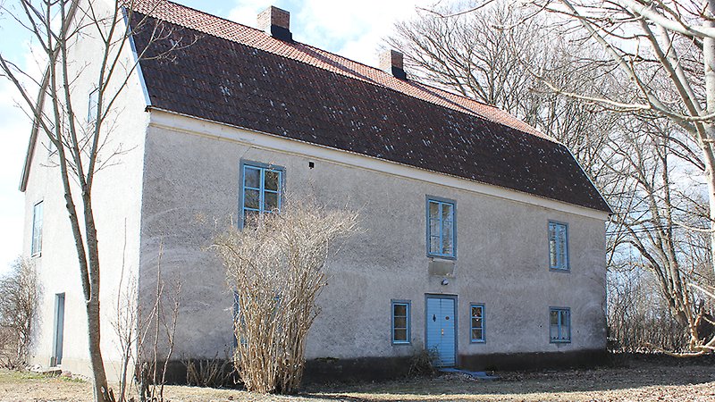 Ett vitt hus av två våningar med blåa fönster och ett rött tak.