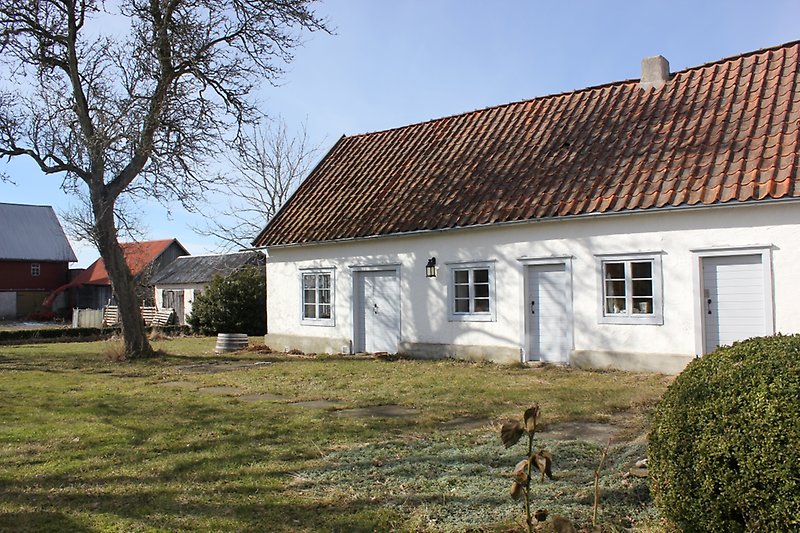 Ett vitt hus med ljusblåa dörrar, ljusblåa fönster och ett rött tegeltak med en skorsten.