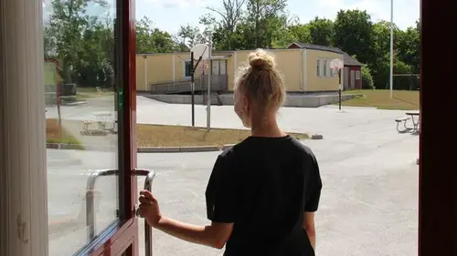Tjej som står i en dörröppning och ser ut mot en skolgård.