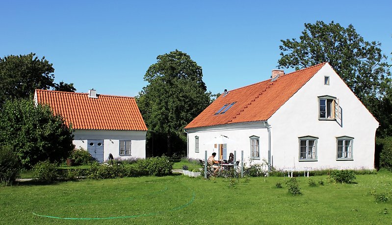 Ett envåningshus med gråa dörrar, gråa fönster och ett rött tegeltak med en skorsten.