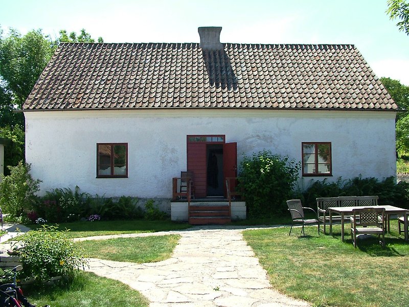 Ett litet vitt hus med en röd ytterdörr, röda fönster och ett rött tak.