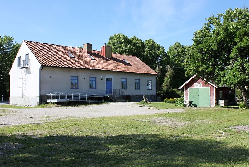 Ett vitt envåningshus med blåa fönster och ett rött tak.