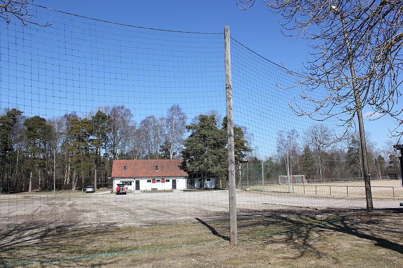Bredvid en fotbollsplan och bakom det upphängda nätet finns en vit envåningsbyggnad.