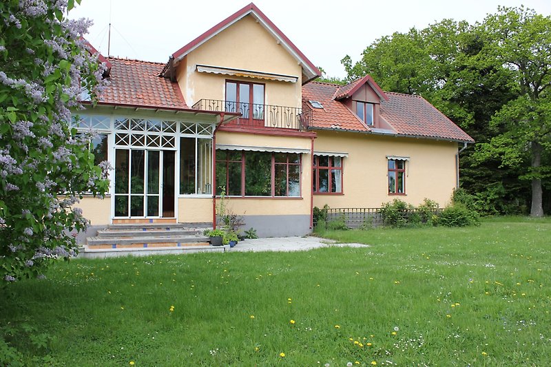Ett gult hus med röda fönster och ett rött tegeltak.